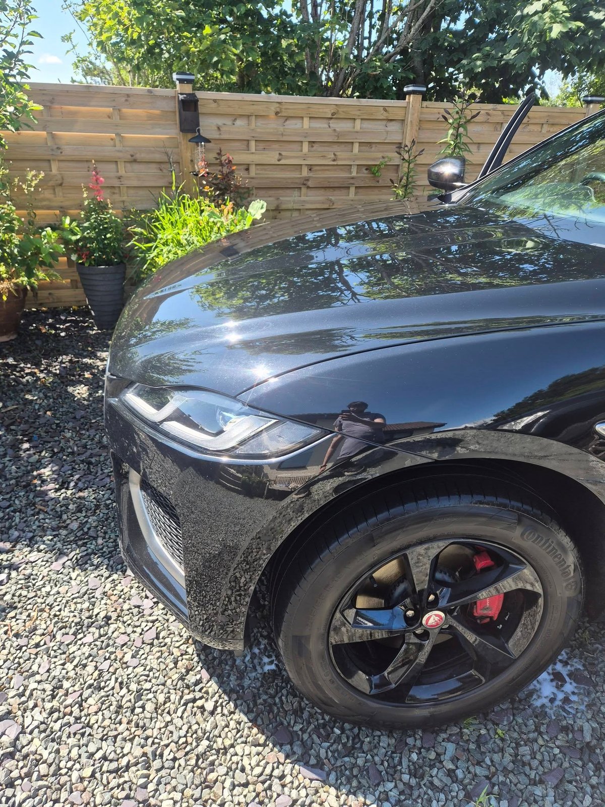 Black car freshly valeted and parked on a gravel driveway in front of a wooden fence